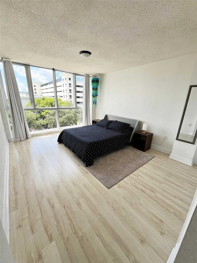 bedroom with a textured ceiling, light hardwood / wood-style flooring, and a wall of windows