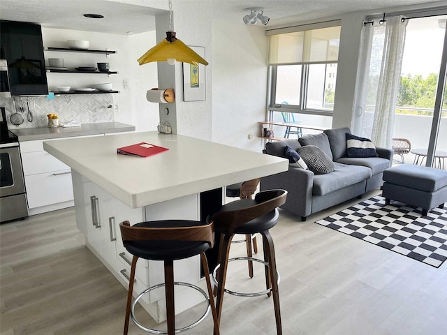 kitchen with stainless steel electric range, a breakfast bar, decorative backsplash, light hardwood / wood-style floors, and white cabinetry