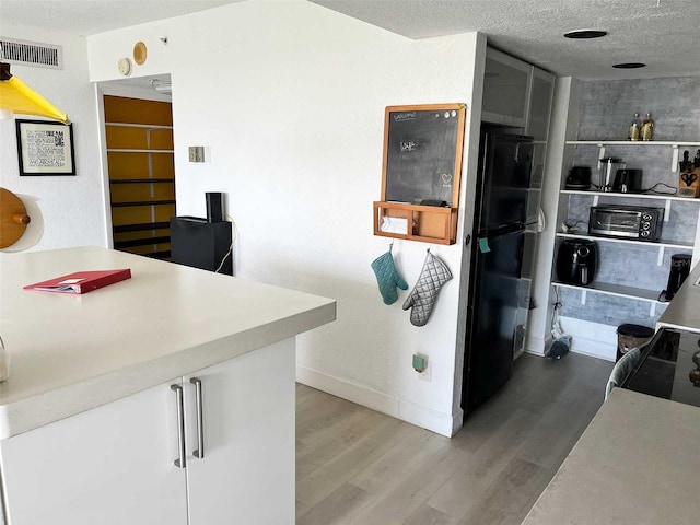 kitchen with white cabinets, wood-type flooring, a textured ceiling, and black fridge