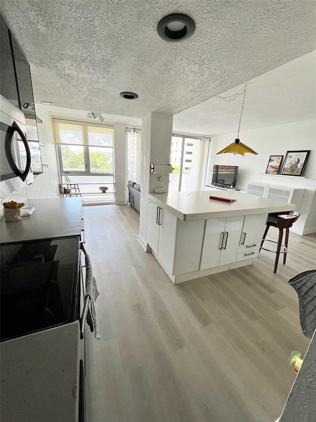 kitchen with white cabinetry, stove, light hardwood / wood-style floors, and a textured ceiling