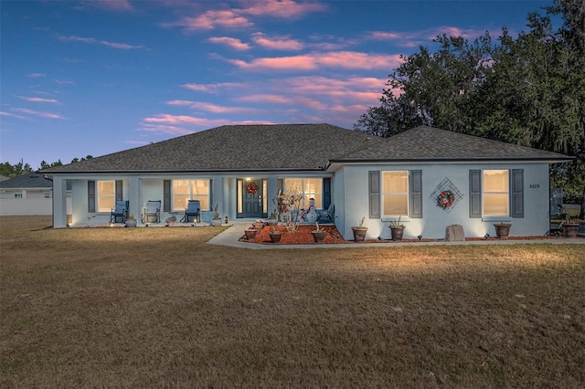 back house at dusk featuring a lawn