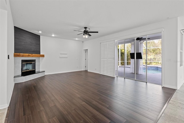 unfurnished living room with dark wood-type flooring, a large fireplace, ceiling fan, and baseboards