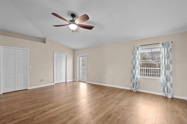 unfurnished bedroom featuring vaulted ceiling, multiple windows, wood finished floors, and baseboards