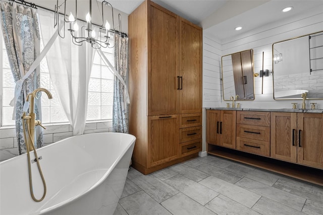 full bath featuring a notable chandelier, double vanity, a soaking tub, decorative backsplash, and a sink