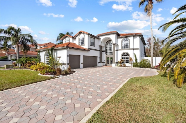 mediterranean / spanish house featuring a tile roof, a front yard, decorative driveway, and stucco siding