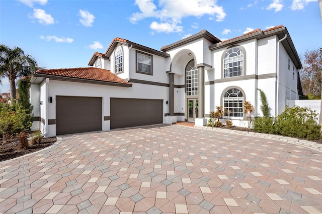 mediterranean / spanish-style house with a tiled roof, an attached garage, decorative driveway, french doors, and stucco siding