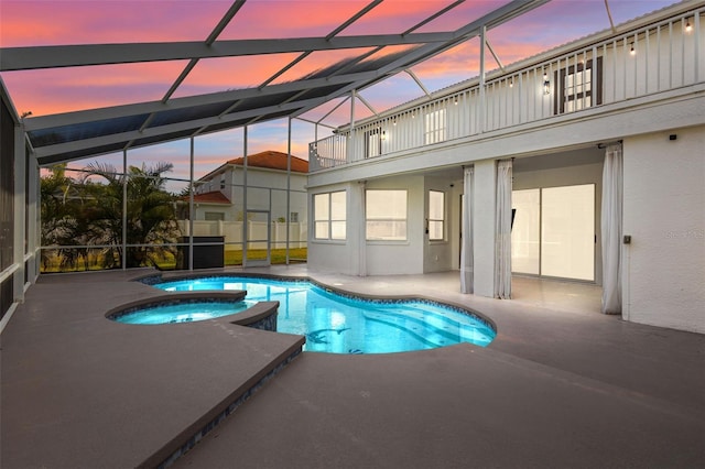 pool at dusk with a pool with connected hot tub, glass enclosure, and a patio