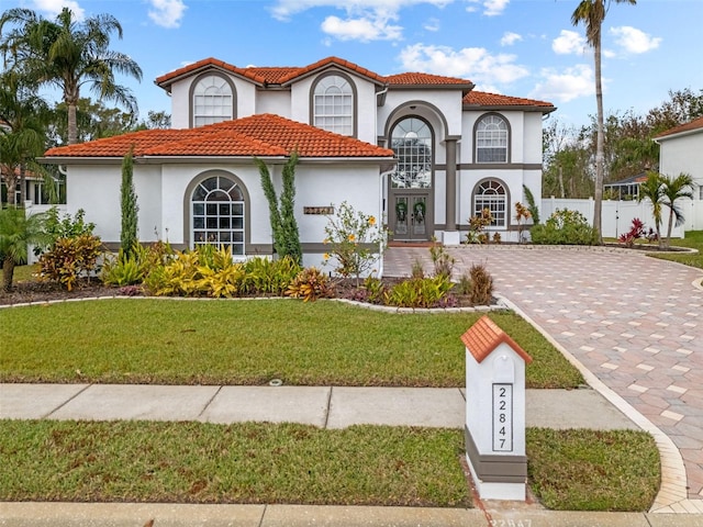 mediterranean / spanish house with a tiled roof, decorative driveway, french doors, a front lawn, and stucco siding