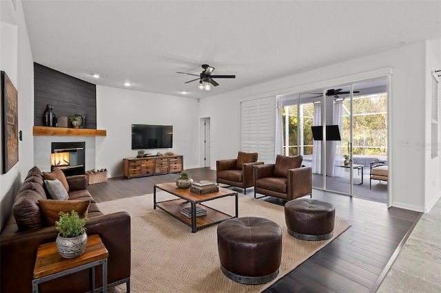 living area featuring a large fireplace, ceiling fan, wood finished floors, and baseboards