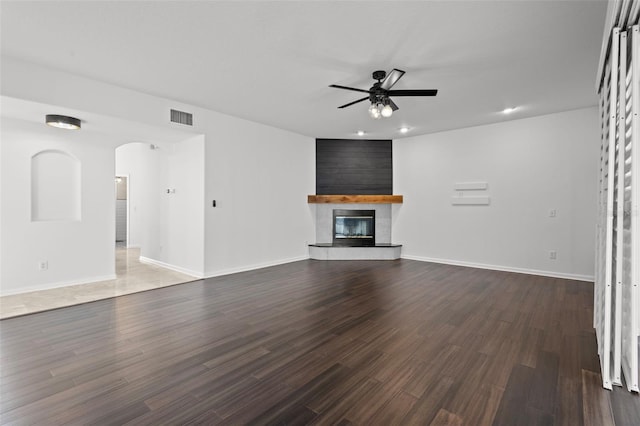 unfurnished living room with dark wood-type flooring, a large fireplace, visible vents, and ceiling fan