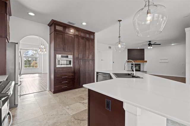 kitchen with arched walkways, decorative light fixtures, light countertops, appliances with stainless steel finishes, and a sink