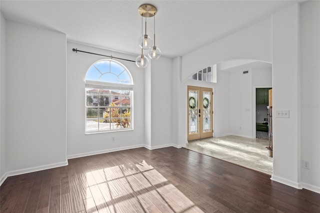 unfurnished dining area with arched walkways, french doors, visible vents, wood finished floors, and baseboards