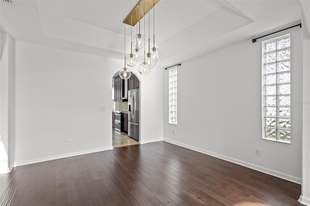 empty room with arched walkways, baseboards, a raised ceiling, and dark wood-type flooring