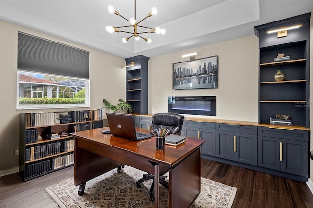 office space featuring dark wood-style floors, a tray ceiling, built in features, and a notable chandelier