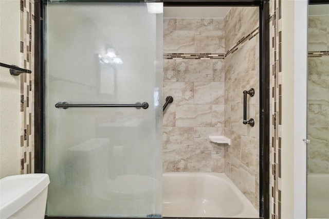 bathroom with toilet and shower / bath combination with glass door