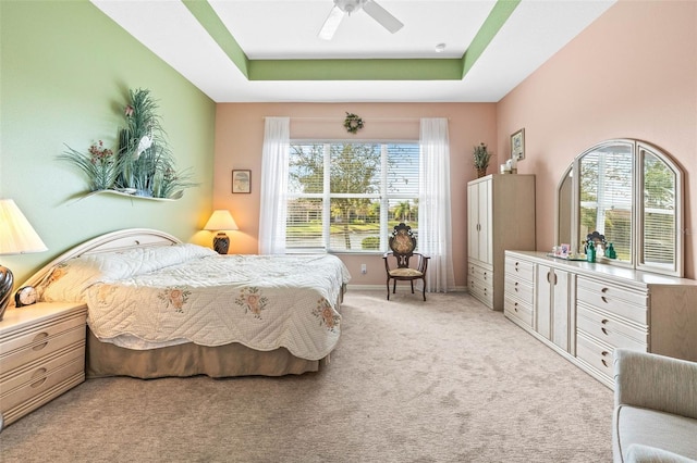 carpeted bedroom featuring ceiling fan, a raised ceiling, and multiple windows