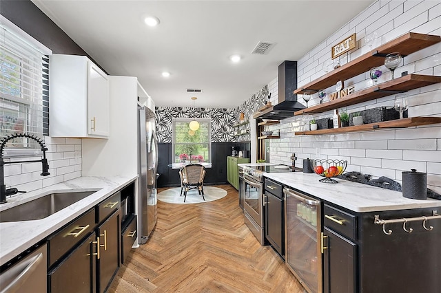 kitchen featuring sink, wall chimney exhaust hood, pendant lighting, white cabinets, and appliances with stainless steel finishes