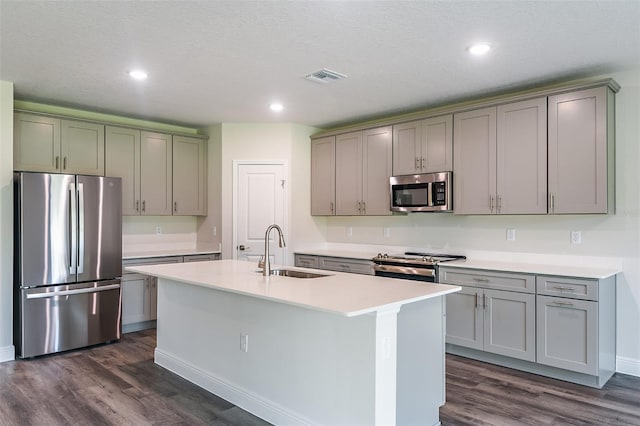 kitchen with a textured ceiling, stainless steel appliances, dark wood-type flooring, sink, and a center island with sink