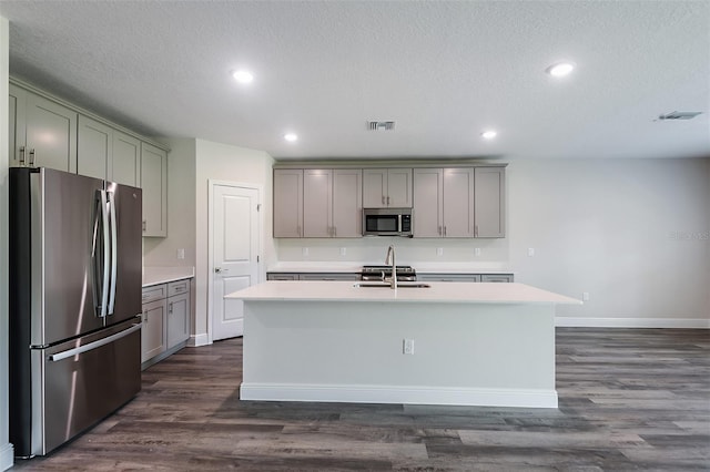 kitchen with sink, stainless steel appliances, dark hardwood / wood-style flooring, a textured ceiling, and a kitchen island with sink