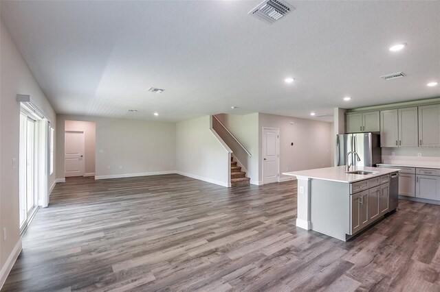 kitchen featuring stainless steel fridge, gray cabinetry, sink, wood-type flooring, and an island with sink