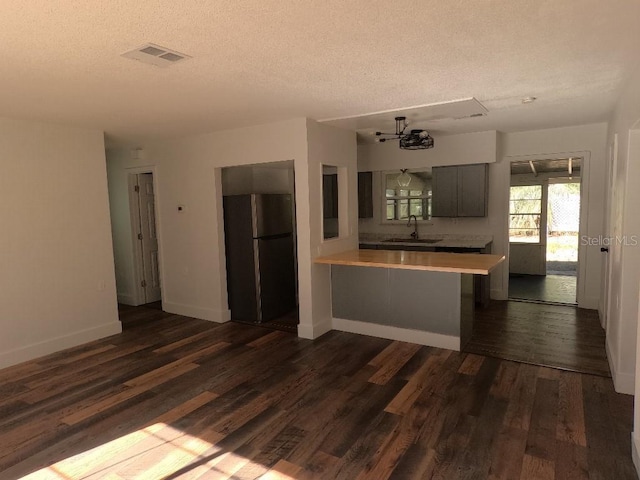 kitchen with sink, a textured ceiling, dark hardwood / wood-style flooring, kitchen peninsula, and stainless steel refrigerator