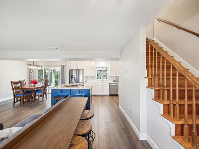 kitchen with white cabinetry, sink, stainless steel appliances, a breakfast bar, and hardwood / wood-style flooring