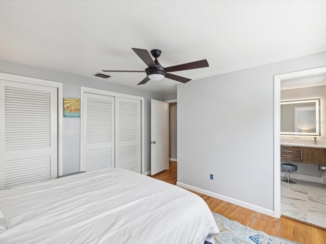 bedroom featuring multiple closets, ceiling fan, hardwood / wood-style floors, and ensuite bathroom