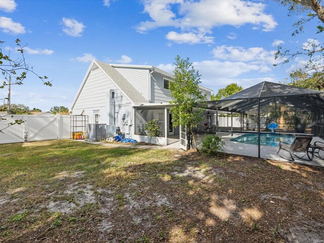 back of property with a lawn, glass enclosure, central AC unit, a fenced in pool, and a patio