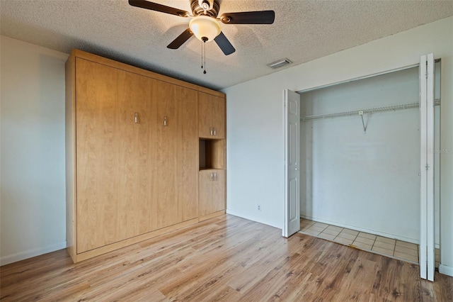 unfurnished bedroom with ceiling fan, a textured ceiling, a closet, and light wood-type flooring