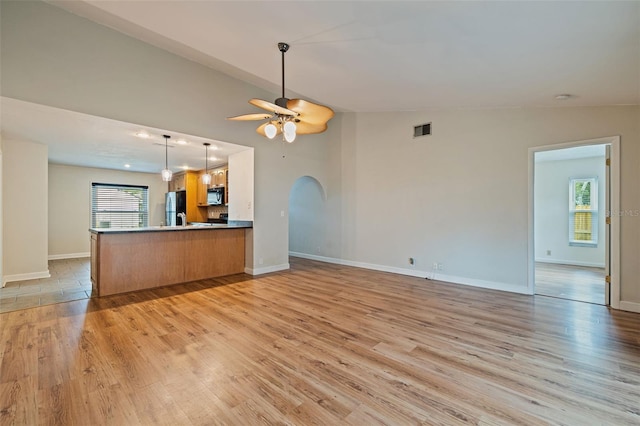 kitchen featuring lofted ceiling, a healthy amount of sunlight, stainless steel fridge, kitchen peninsula, and ceiling fan