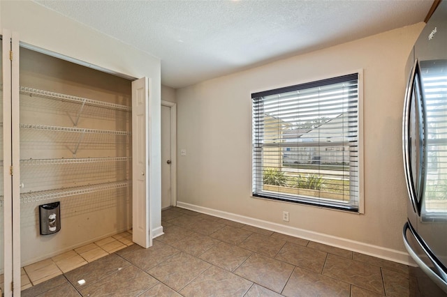 unfurnished bedroom featuring a closet, stainless steel refrigerator, a textured ceiling, and tile patterned flooring