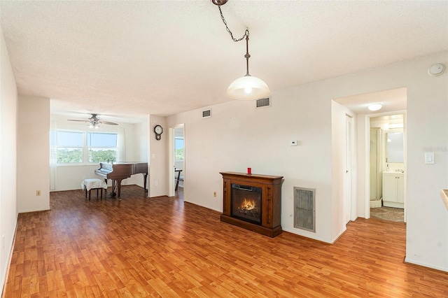 unfurnished living room featuring ceiling fan, a textured ceiling, and light wood-type flooring