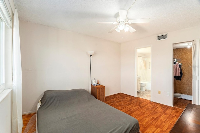 bedroom featuring ceiling fan, ensuite bath, wood-type flooring, and a textured ceiling