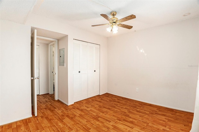 unfurnished bedroom featuring light hardwood / wood-style flooring, a textured ceiling, electric panel, a closet, and ceiling fan