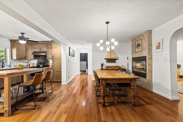 dining room featuring a fireplace, light hardwood / wood-style flooring, ceiling fan with notable chandelier, and a textured ceiling