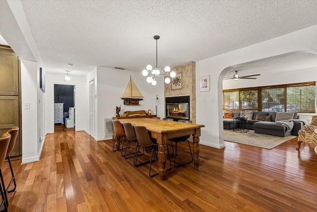 dining room with hardwood / wood-style flooring, ceiling fan with notable chandelier, a fireplace, and a textured ceiling