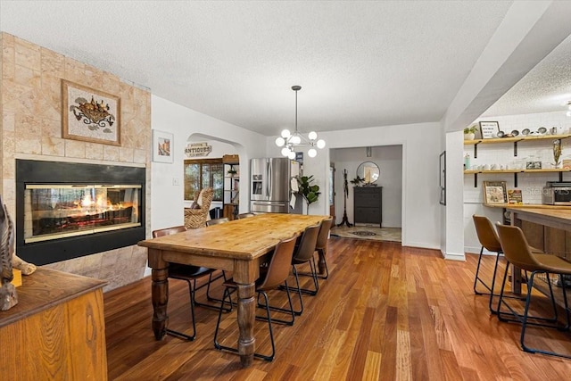 dining space with a tiled fireplace, a chandelier, a textured ceiling, and hardwood / wood-style flooring