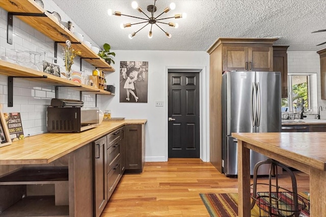 kitchen with a textured ceiling, light wood-type flooring, butcher block countertops, and stainless steel refrigerator