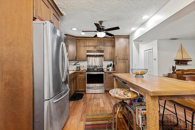 kitchen featuring tasteful backsplash, a textured ceiling, stainless steel appliances, ceiling fan, and light hardwood / wood-style flooring