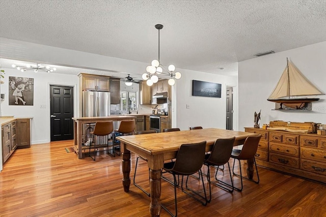 dining space with ceiling fan, light wood-type flooring, and a textured ceiling