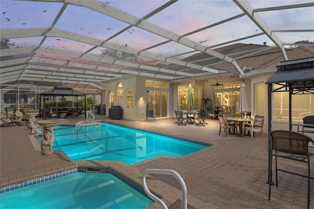 pool at dusk with an in ground hot tub, glass enclosure, and a patio area