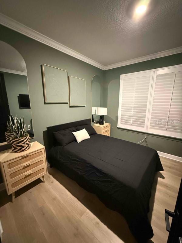 bedroom with a textured ceiling, light hardwood / wood-style flooring, and ornamental molding