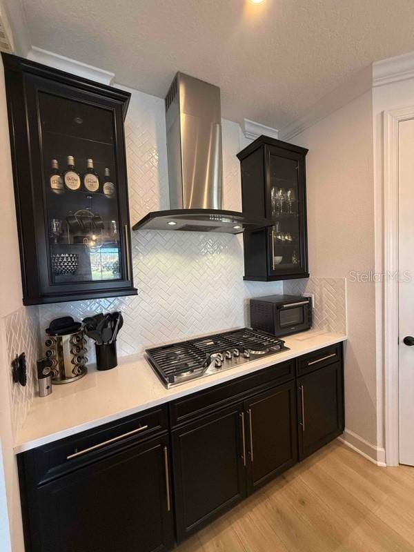 kitchen featuring light wood-type flooring, stainless steel gas stovetop, wall chimney exhaust hood, and backsplash