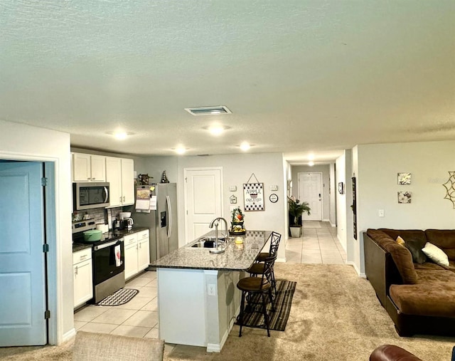 kitchen featuring a center island with sink, white cabinets, sink, a kitchen bar, and stainless steel appliances