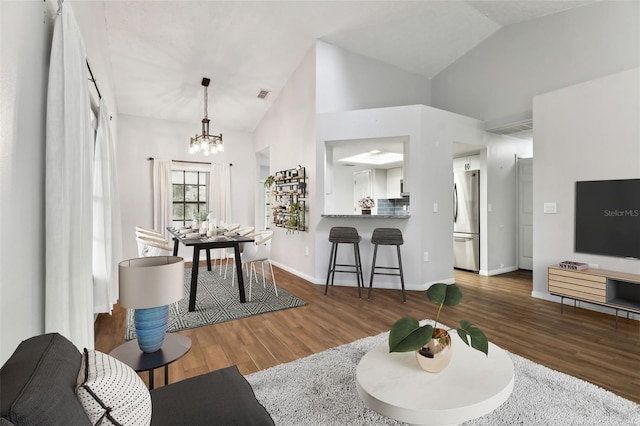 living room with a chandelier, dark wood-type flooring, and vaulted ceiling