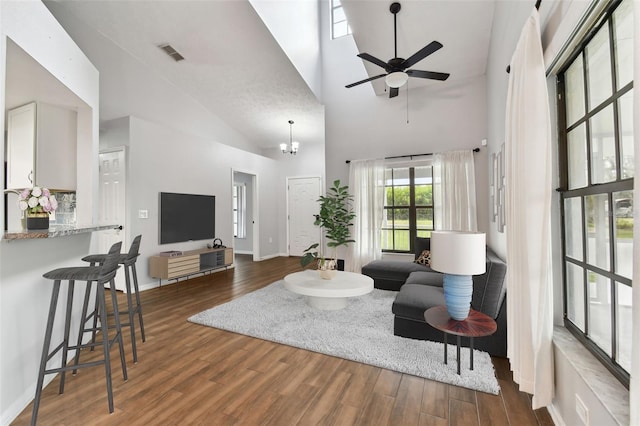 living room with ceiling fan with notable chandelier, dark hardwood / wood-style flooring, and high vaulted ceiling