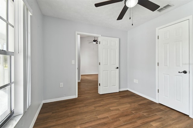 unfurnished bedroom featuring dark hardwood / wood-style floors, ceiling fan, a textured ceiling, and multiple windows