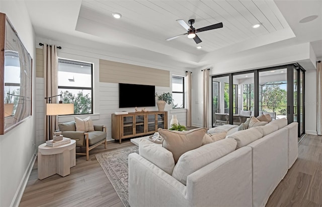 living room with ceiling fan, a tray ceiling, wooden walls, wood ceiling, and light wood-type flooring