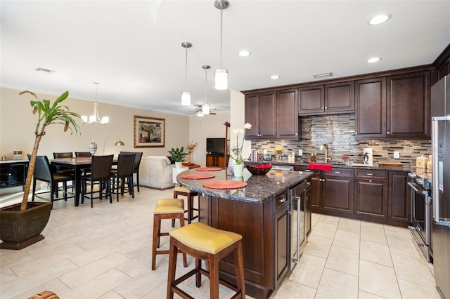 kitchen with a kitchen bar, appliances with stainless steel finishes, ceiling fan with notable chandelier, decorative light fixtures, and dark stone countertops