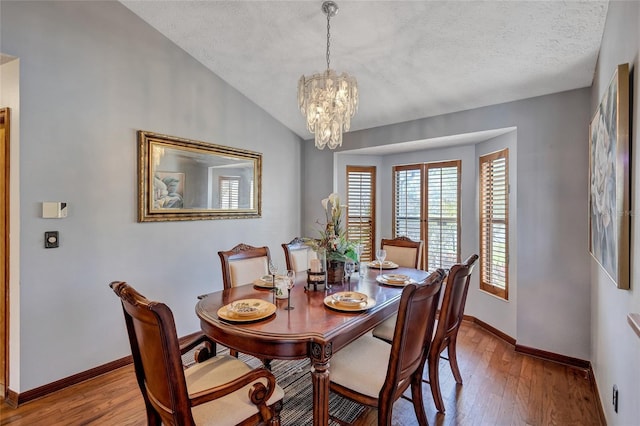 dining space featuring light hardwood / wood-style floors, vaulted ceiling, a textured ceiling, and an inviting chandelier